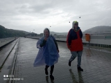 Dwie osoby w płaszczach przeciwdeszczowych spacerujące  po deptaku na zaporze solińskiej
