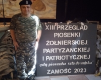 mężczyzna pozuje przy banerze informacyjnym XII Przegląd Piosenki Żołnierskiej, Partyzanckiej i Patriotycznej